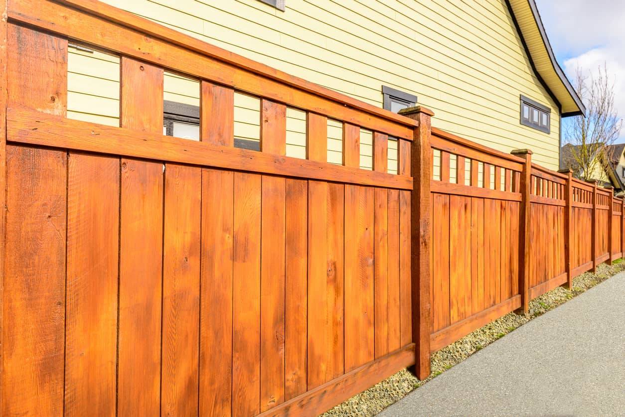This picture shows a stained wooden fence in front of a house.