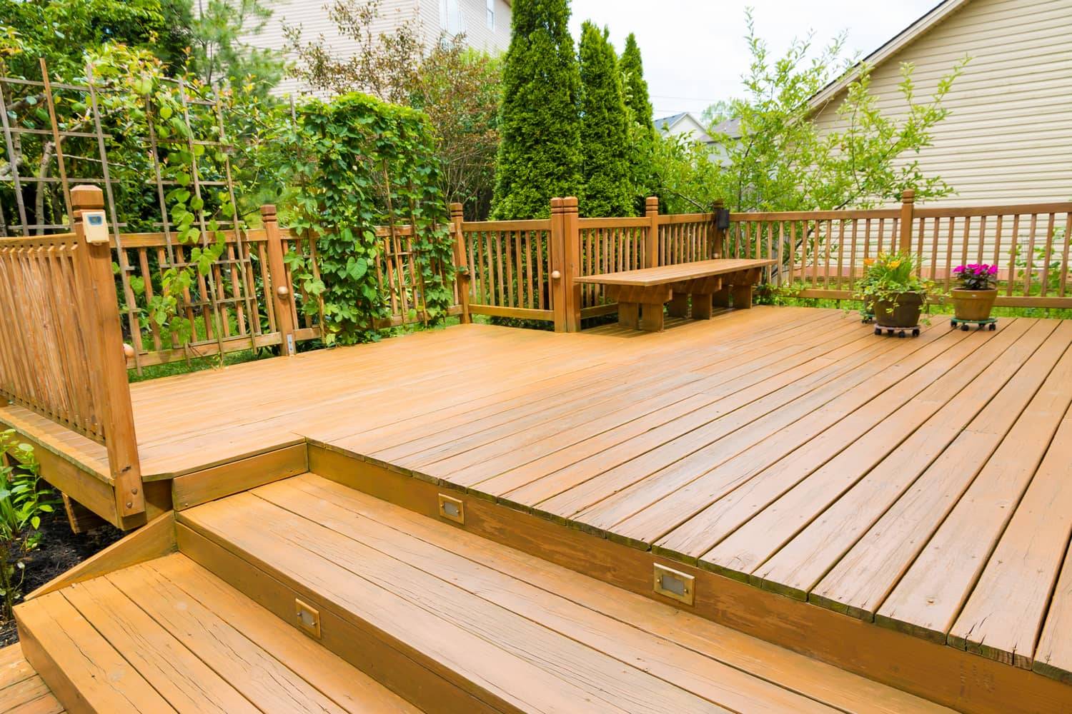 This picture is of a large wooden deck with a bench next to a garden.
